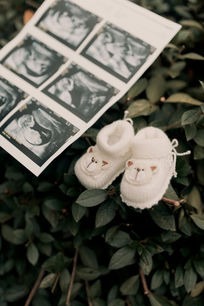 pexels-photo-31627496-31627496 A pair of baby shoes next to an ultrasound image on green leaves, symbolizing motherhood and new beginnings.